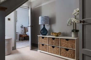 A hallway with a white console table, wicker baskets, a blue vase, and white orchids. - 4 Bed in The Lizard (oc-b620048) (Coverack)