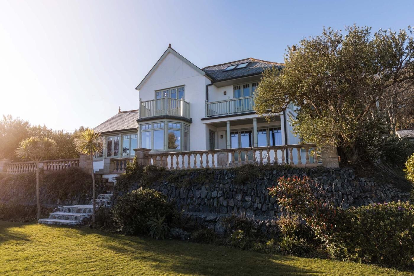 A two-story house with a stone retaining wall, a balcony, and a well-maintained lawn.