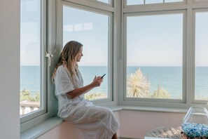 Eine Person sitzt am Fenster mit Blick auf das Meer.