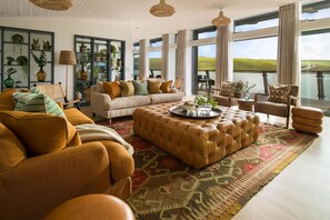 A spacious living room with a large window, a sofa set, a coffee table, and a rug. - 4 Bed in Watergate Bay (oc-b584345) (Tregurrian)