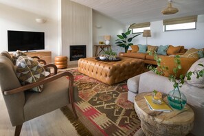 A living room with a sofa, armchair, ottoman, and a flat-screen TV. - 4 Bed in Watergate Bay (oc-b584345) (Tregurrian)