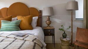 A neatly made bed with a headboard, a bedside table with a lamp, a small side table with a vase, and a chair. - 4 Bed in Watergate Bay (oc-b584345) (Tregurrian)