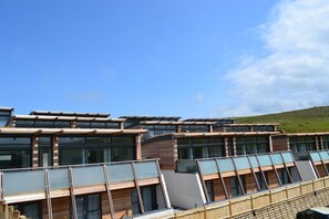 A modern building with multiple levels, large windows, and a flat roof. - 4 Bed in Watergate Bay (oc-b584345) (Tregurrian)