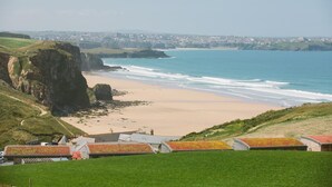 Paisagem costeira com praia, falésias e vista para uma cidade ao longe.