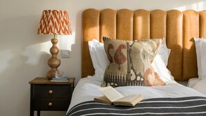 Quarto de hotel com cama, mesa de cabeceira com abajur e um livro na cama.