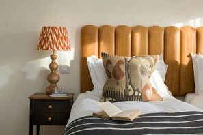 A hotel room with a bed, a nightstand with a lamp, and a book on the bed. - 4 Bed in Watergate Bay (oc-b584373) (Tregurrian)