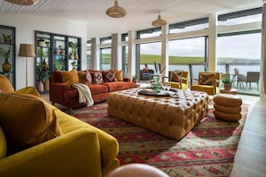 A spacious living room with a large window, a sofa set, and a patterned rug. - 4 Bed in Watergate Bay (oc-b584373) (Tregurrian)