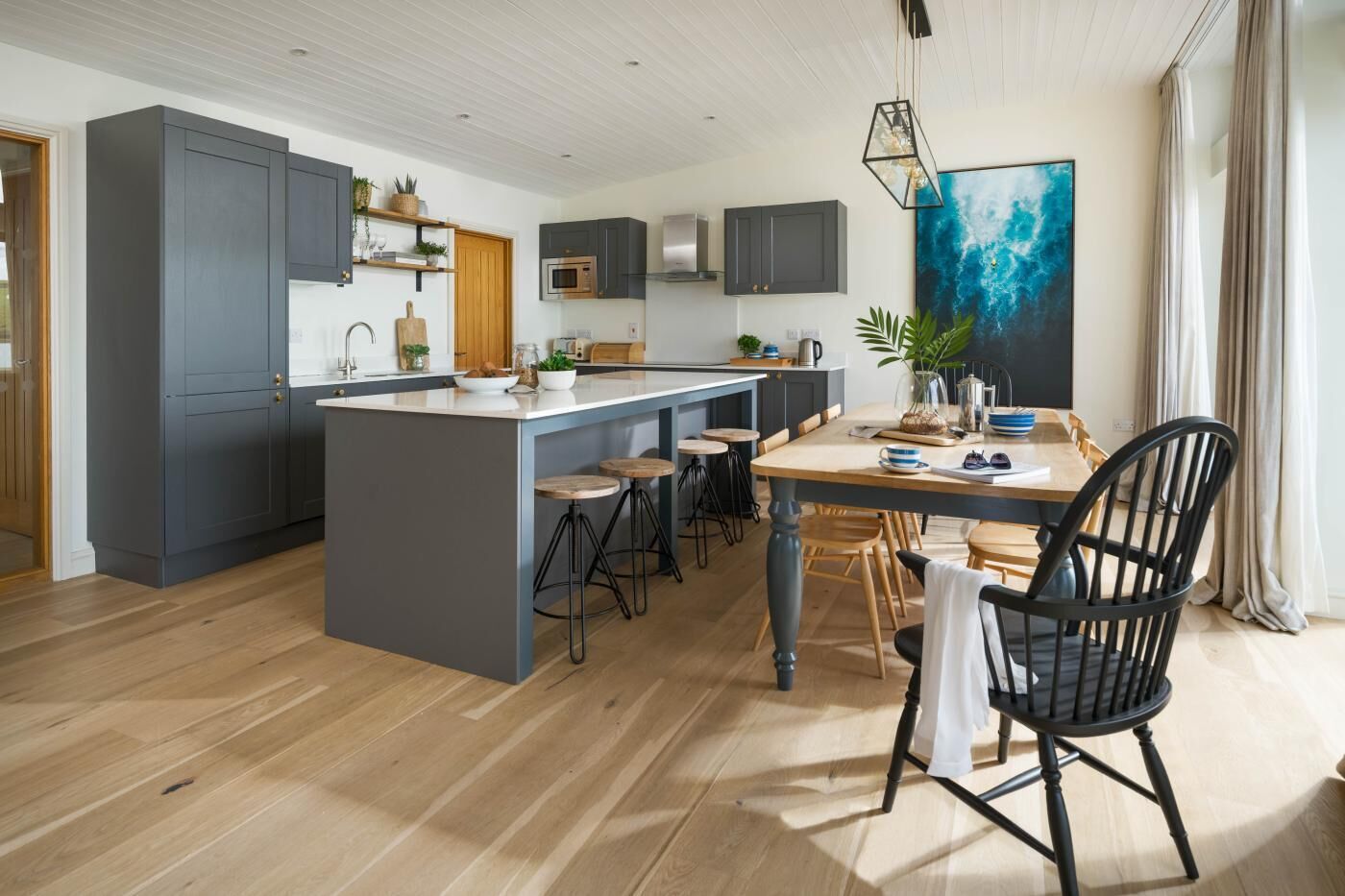 A modern kitchen with a central island, bar stools, and a dining table with chairs.