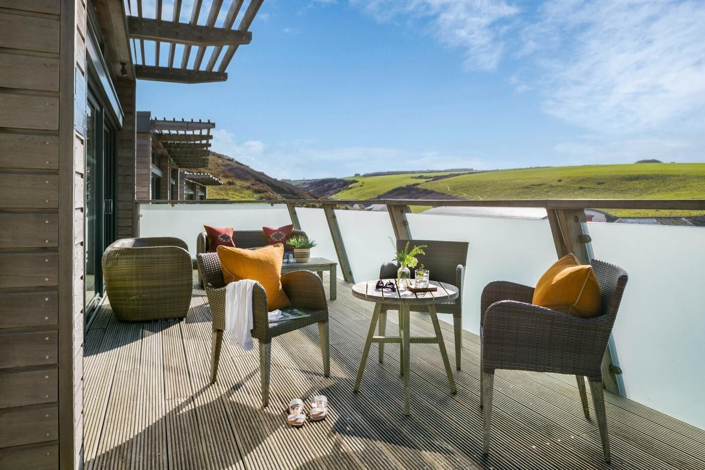 A deck with wicker furniture, a table, and a view of a green landscape.