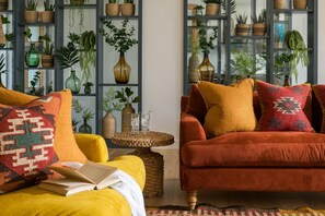 Ein gemütliches Wohnzimmer mit einem roten Sofa, einem gelben Sessel und einem mit Pflanzen gefüllten Bücherregal.
