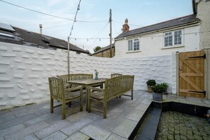 Une terrasse avec une table et des chaises en bois, un mur blanc et un portail en bois.
