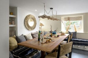 Un coin repas avec une table en bois, des chaises en osier et un grand miroir au mur.
