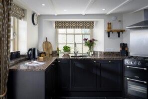 A modern kitchen with black cabinets, a granite countertop, a stove, and a window with a view. - 5 Bed in Porth (oc-b584392) (Newquay)