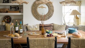 A dining area with a wooden table, woven chairs, and a woven wall hanging. - 5 Bed in Porth (oc-b584392) (Newquay)