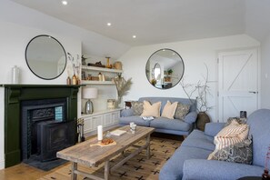 A living room with a fireplace, a sofa set, a coffee table, and two round mirrors. - 5 Bed in Porth (oc-b584392) (Newquay)