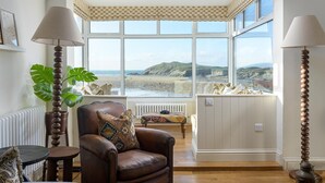 A room with a view of the beach, a leather armchair, a table, and two lamps. - 5 Bed in Porth (oc-b584392) (Newquay)