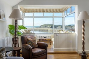 A room with a view of the beach, a leather armchair, a table, and two lamps. - 5 Bed in Porth (oc-b584392) (Newquay)