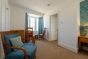 Ein Zimmer mit großem Fenster, einem Holzstuhl, einem kleinen Tisch und einer Tür zu einem anderen Raum.