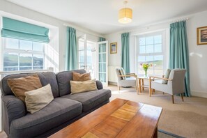 Ein Wohnzimmer mit einer Couch, einem Couchtisch, einem Sessel und Blick ins Freie.