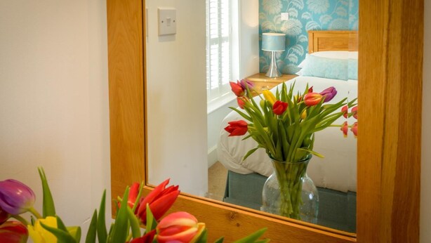 A bedroom with a bed, a nightstand, a lamp, and a vase of tulips in the foreground. - 2 Bed in Porth (oc-b584410) (Newquay)