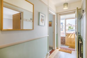 A hallway with a wooden door, a mirror, and a framed picture on the wall. - 3 Bed in Southwold (oc-hseami) (Southwold)