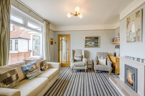 A living room with a sofa, armchairs, a fireplace, and a view of the outside. - 3 Bed in Southwold (oc-hseami) (Southwold)
