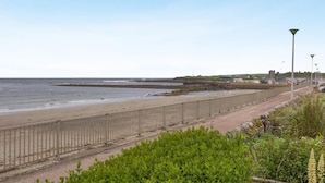 A coastal road with a metal fence, a beach, and a distant castle-like structure. - 2 Bed in Thurso (oc-n41742) (Thurso)