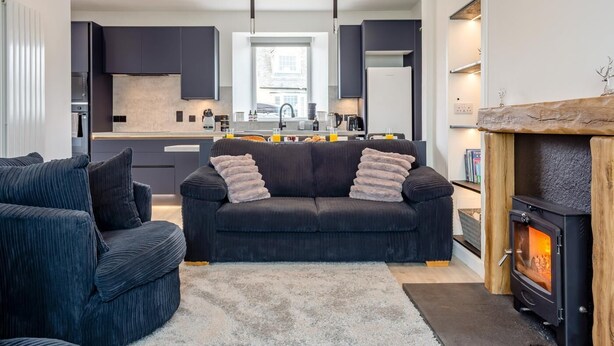 A modern living room with a sofa, a fireplace, and a kitchen in the background. - 2 Bed in Thurso (oc-n41742) (Thurso)