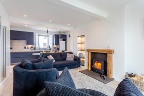 Ein modernes Wohnzimmer mit Kamin, einer Couch und einer Küchenzeile im Hintergrund.