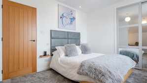 A bedroom with a wooden door, a grey upholstered headboard, a white bed with grey pillows, a fluffy grey blanket, and a wall-mounted abstract painting. - 2 Bed in Thurso (oc-n41742) (Thurso)
