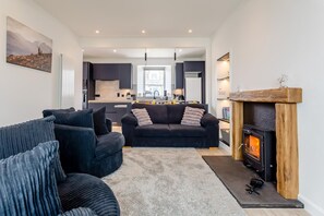 Ein modernes Wohnzimmer mit Kamin, einer Sofagarnitur und einer Küche im Hintergrund.