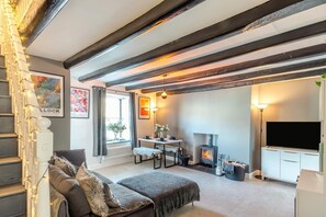 Ein gemütliches Zimmer mit sichtbaren Holzbalken, Kamin, Fernseher und Essbereich.