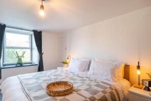 Ein Schlafzimmer mit Bett, Nachttisch, Lampe und Fenster mit Vorhängen.