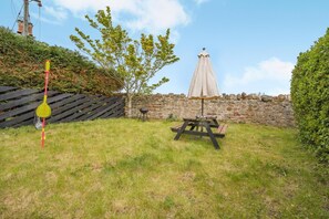 A grassy backyard with a picnic table, a barbecue grill, and a wooden fence. - 2 Bed in Dunbar (oc-t42811) (Innerwick)