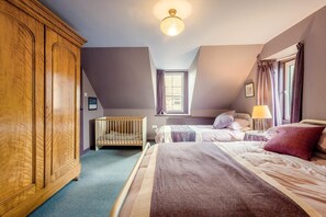 A bedroom with a wooden wardrobe, a crib, two beds with pillows, a bedside lamp, and a window with curtains. - 2 Bed in Dunbar (oc-t42811) (Innerwick)