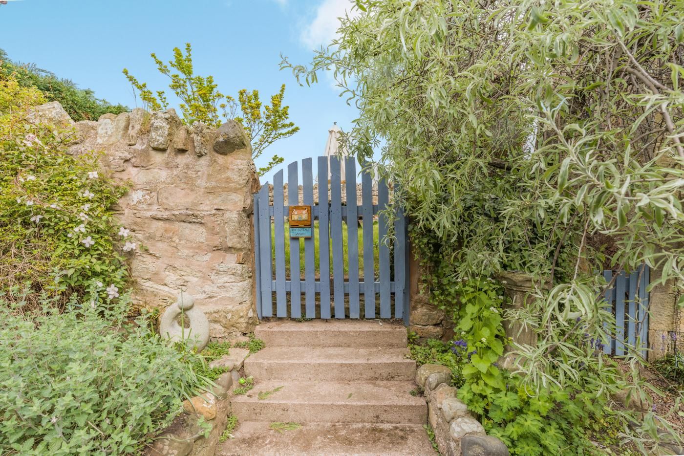 A stone wall with a wooden gate leading to a garden.