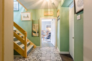 A hallway with a wooden staircase, patterned floor tiles, and a door leading to a room with a blue chair and bookshelves. - 2 Bed in Dunbar (oc-t42811) (Innerwick)