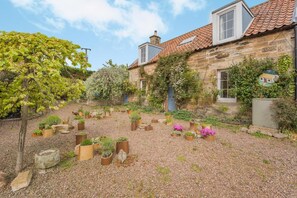 A stone building with a tiled roof, surrounded by a gravel courtyard with potted plants. - 2 Bed in Dunbar (oc-t42811) (Innerwick)
