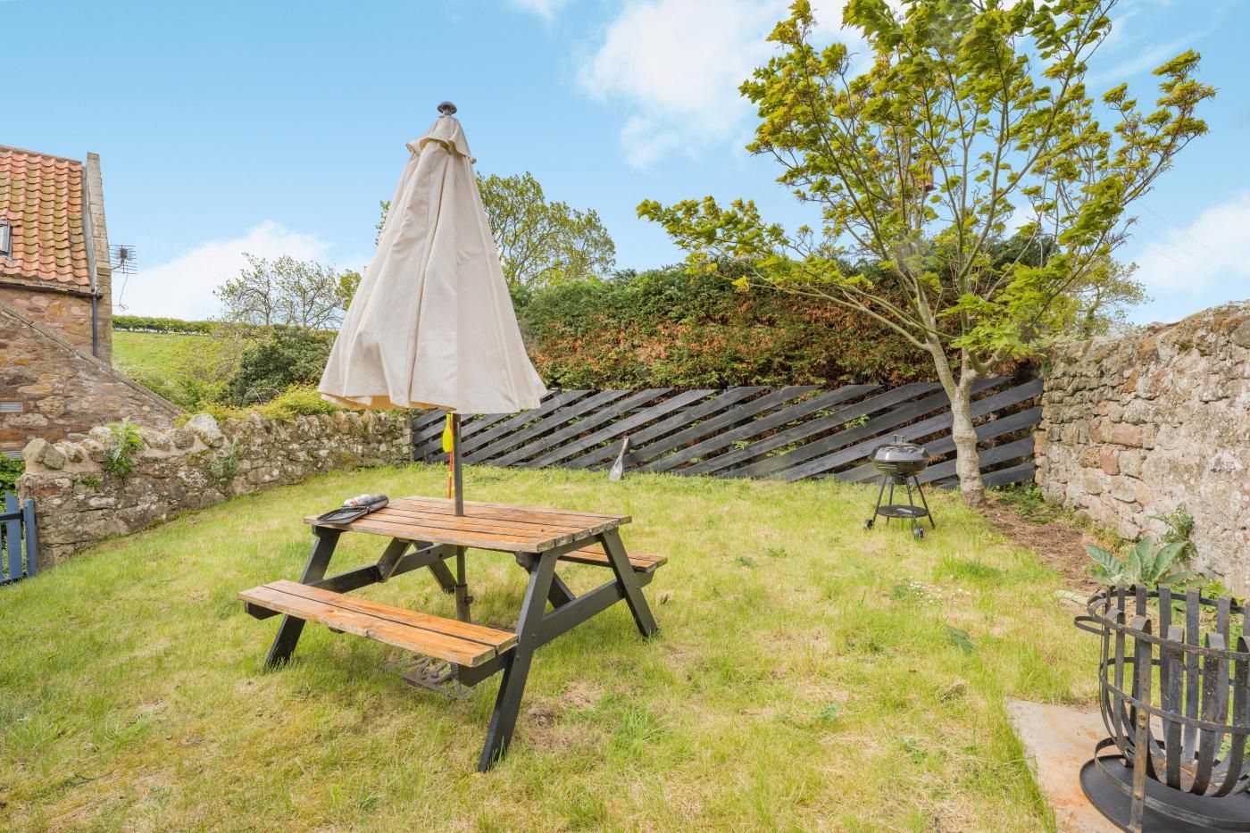 A picnic table with a canopy, a barbecue grill, and a stone wall in a grassy backyard.