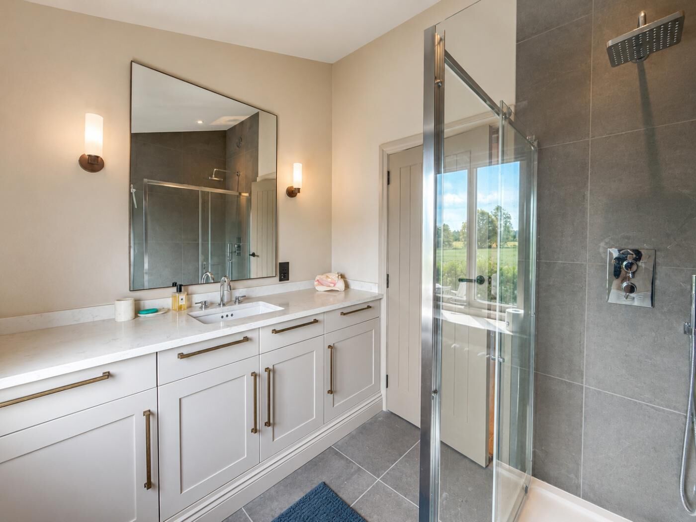 A modern bathroom with a glass shower enclosure, a large mirror, and a white vanity with a sink.