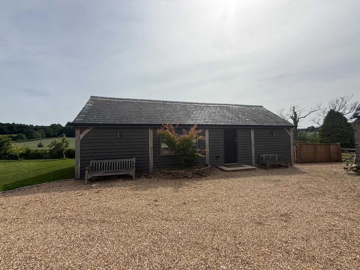 A single-story building with a gravel driveway, a wooden bench, and a small tree in front.