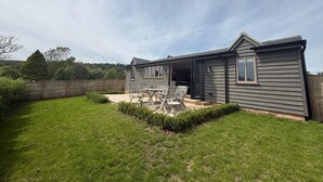Ein zweistöckiges Haus mit einer Terrassenfläche, einem eingezäunten Garten und Blick auf die umliegende Landschaft.