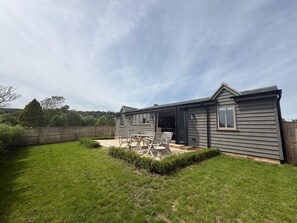 Ein zweistöckiges Haus mit einer Terrassenfläche, einem eingezäunten Garten und Blick auf die umliegende Landschaft.