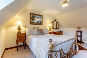 A bedroom with a large bed, two bedside tables with lamps, a dresser, a mirror, and a small statue on a side table. - 2 Bed in Ballater (oc-o45326) (Ballater)