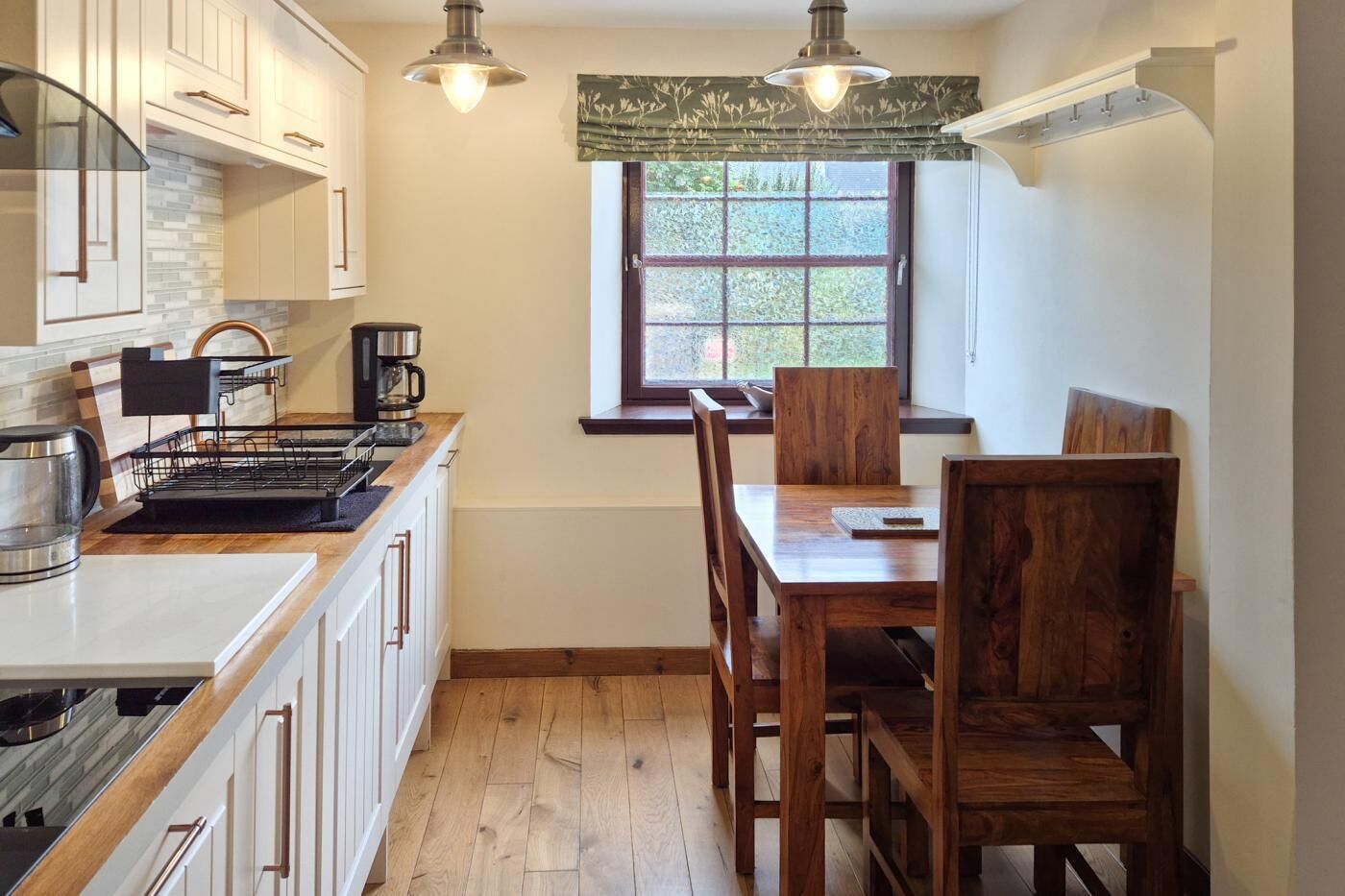 A kitchen with white cabinets, a wooden dining table, and a window with a view of greenery.