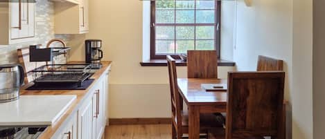A kitchen with white cabinets, a wooden dining table, and a window with a view of greenery.