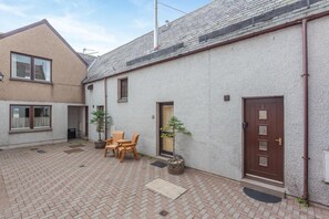 A residential building with a paved courtyard, wooden furniture, and potted plants. - 2 Bed in Ballater (oc-o45326) (Ballater)