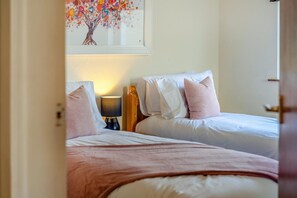 Habitación de hotel con dos camas, una mesita de noche con lámpara y un cuadro de un árbol con corazones en la pared.