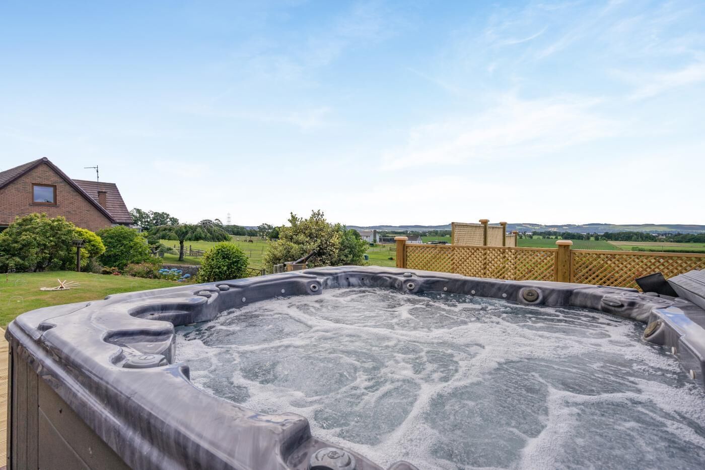 Un bain à remous dans un jardin, avec vue sur une maison en briques et une clôture en bois.