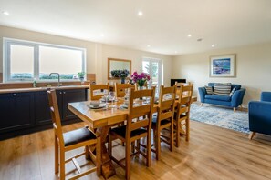 Un comedor con mesa y sillas de madera, una cocina con armarios oscuros, y una sala de estar con un sofá azul y una alfombra.